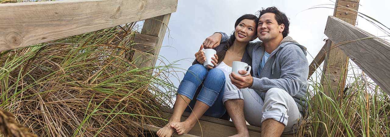 Photo of a young couple sitting on a beach drinking coffee.