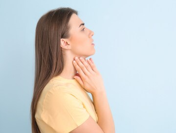 A woman touching her throat to feel for lumps, a sign of neck cancer.